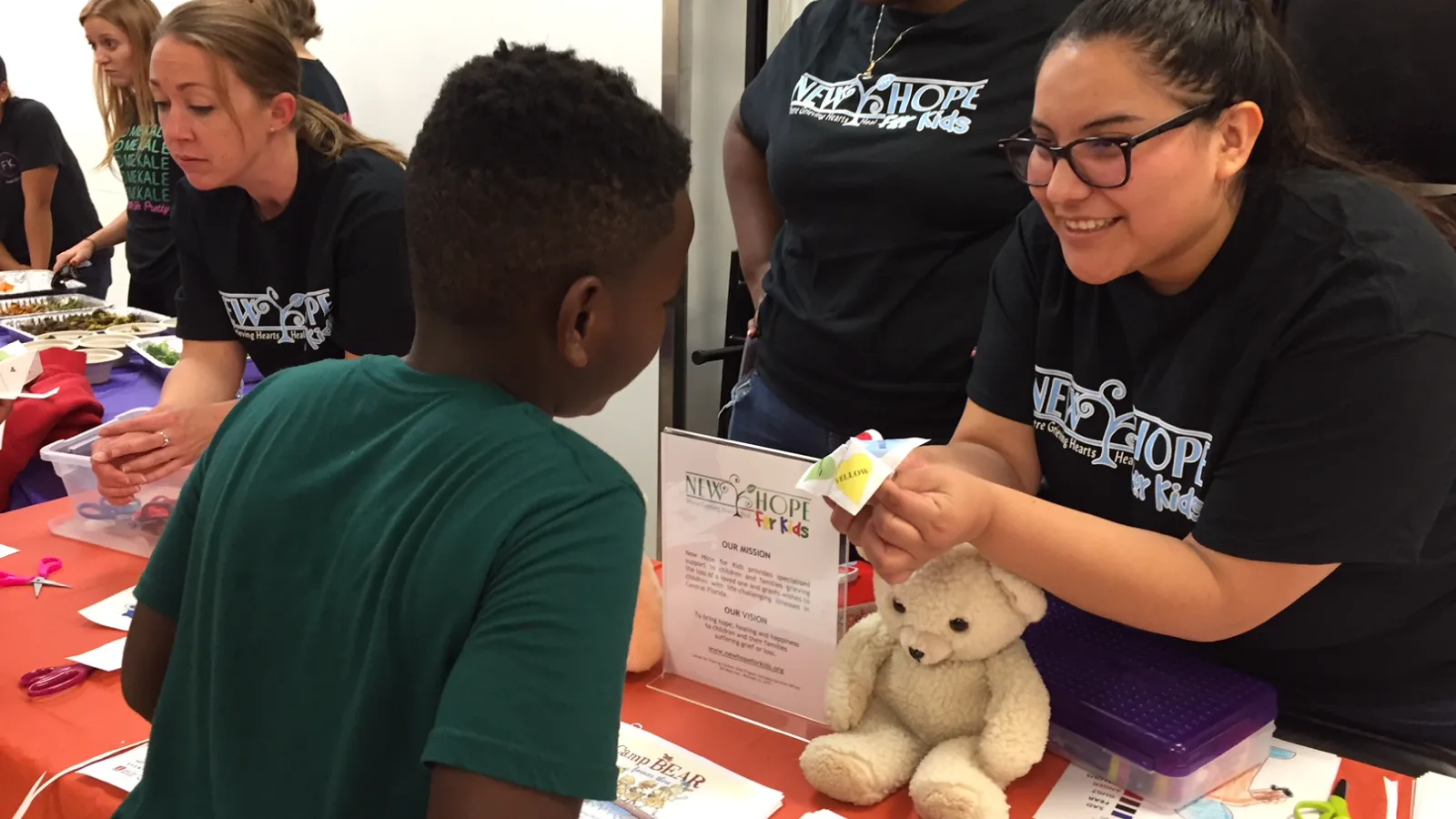 New Hope for Kids staff member giving a stuffed animal bear to a child